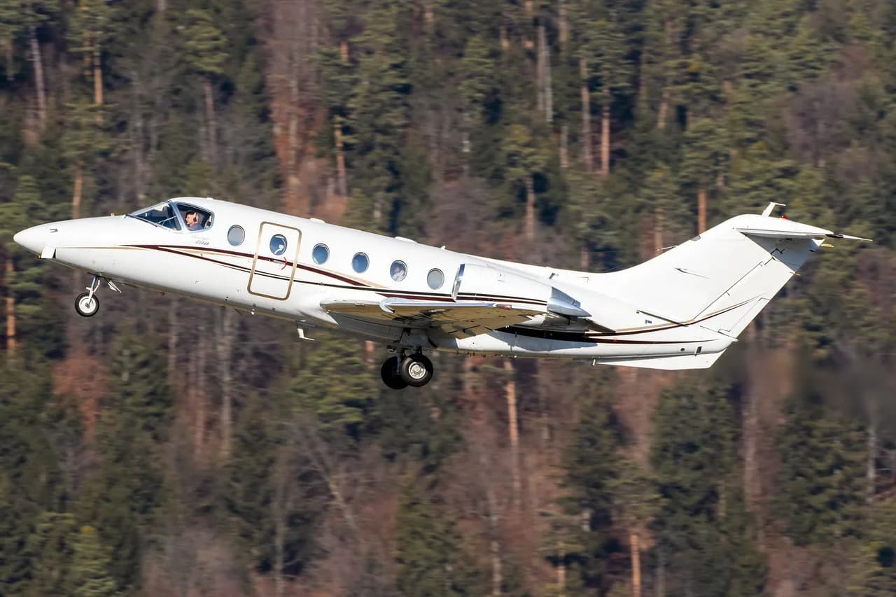 A Hawker Beechcraft Premier I taking off with trees in the background.