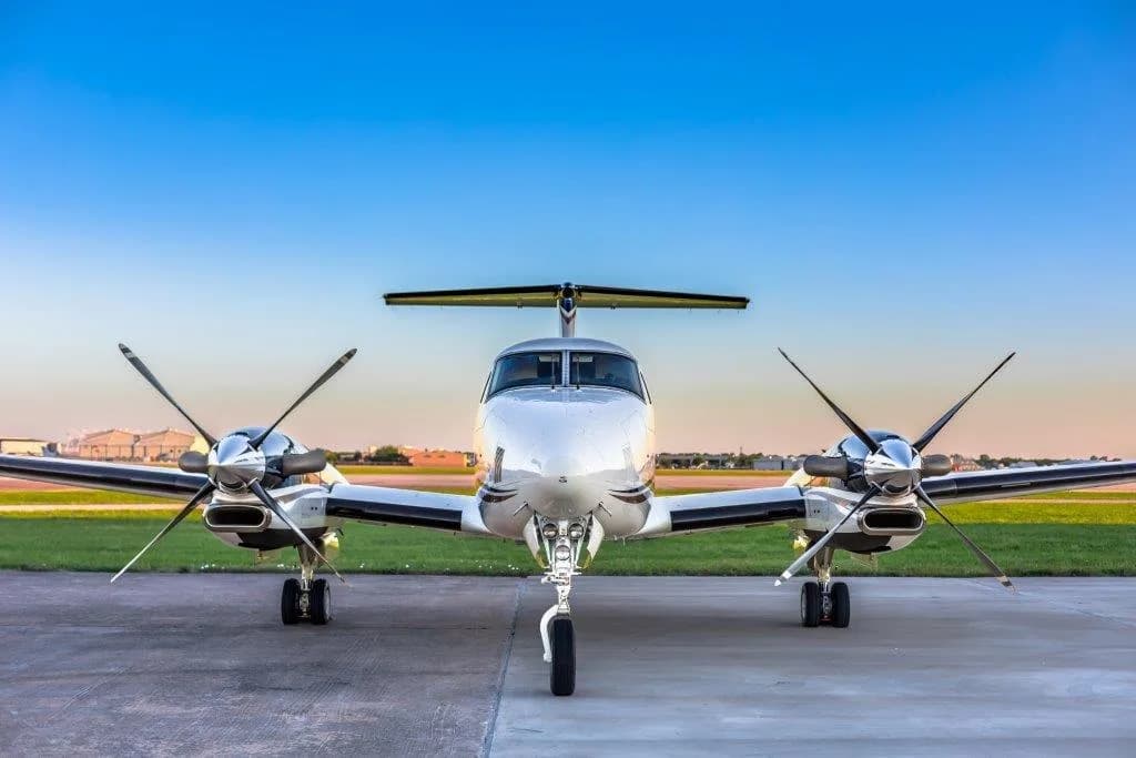A white and black Beechcraft King Air 350i turboprop aircraft parked on an airfield, viewed from the front.