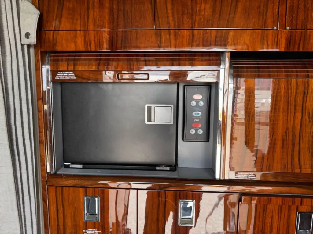Close-up of a built-in microwave oven and control panel within the polished dark wood cabinetry of a business jet galley.