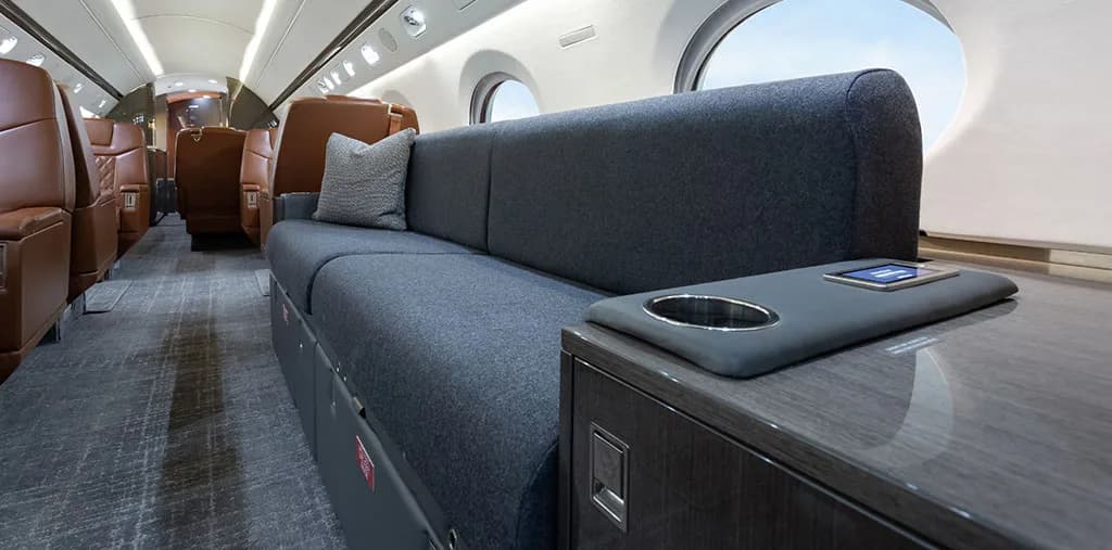 A close-up of the grey sofa and a side table with a cup holder and control panel in the aircraft cabin.