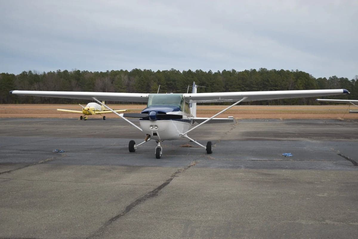 A white Cessna 172 with blue and grey stripes is parked on a tarmac, viewed from the front.