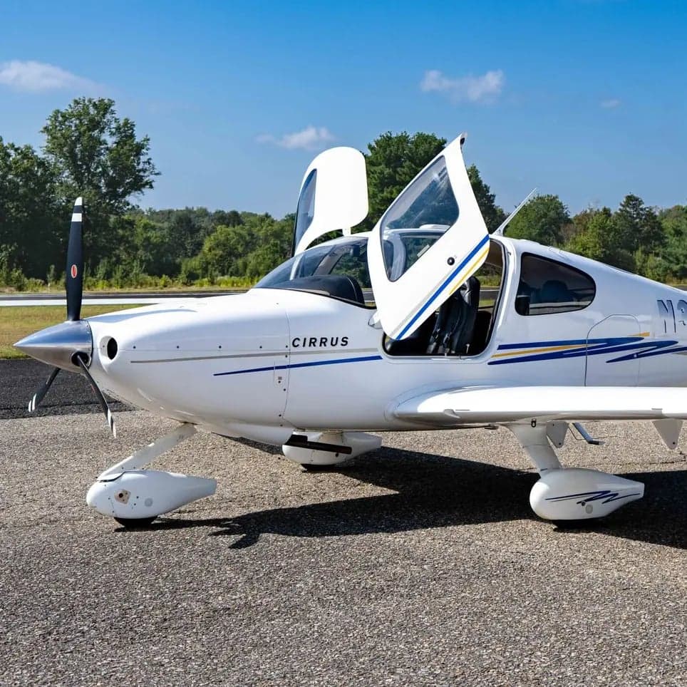 Cirrus SR22 with white paint scheme and open gull-wing door on the tarmac.