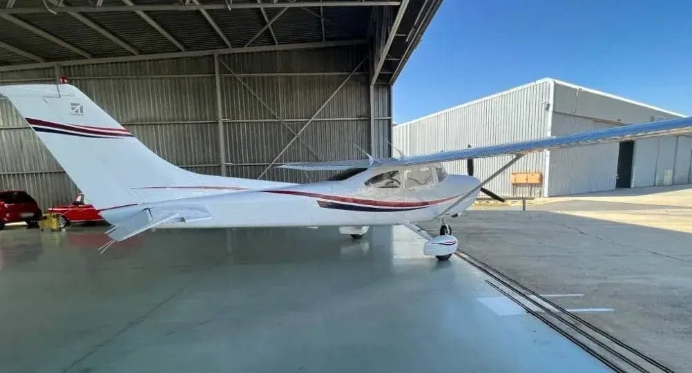 Side view of a Cessna aircraft parked inside a hangar, featuring its white paint scheme with red and blue accents.