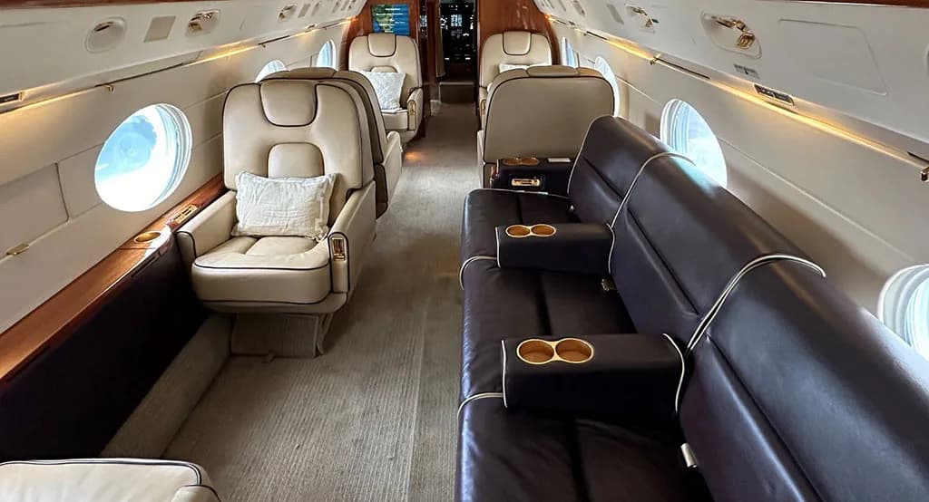 A view of a private jet cabin featuring beige leather seats and a dark brown leather sofa.