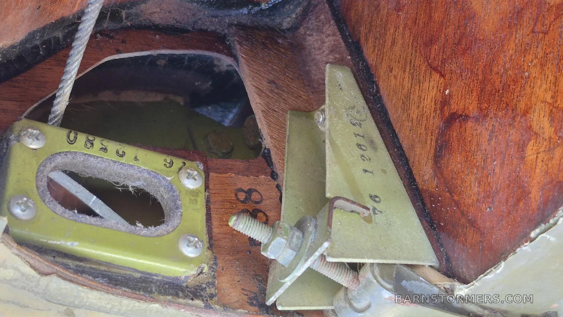 A close-up view of internal aircraft structure, showing wooden ribs, metal brackets, bolts, and a control cable.