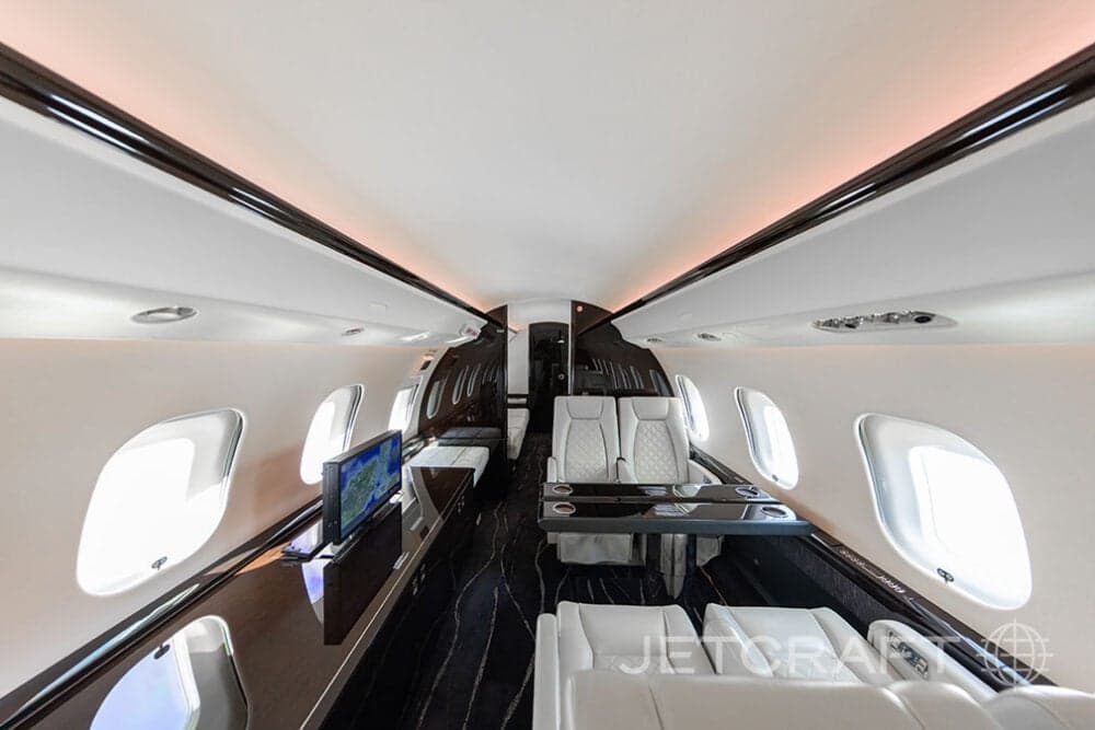 Aft view of the cabin of a Bombardier Global Express with white leather seats, tables, and a monitor.