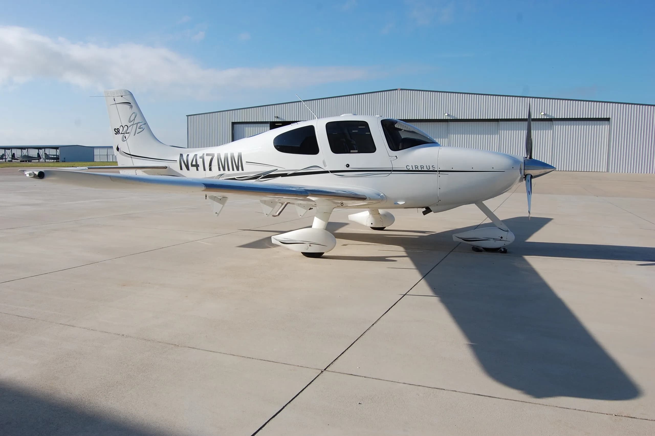 A three-quarter front view of the white Cirrus SR22 aircraft, N417MM, parked on an airfield.