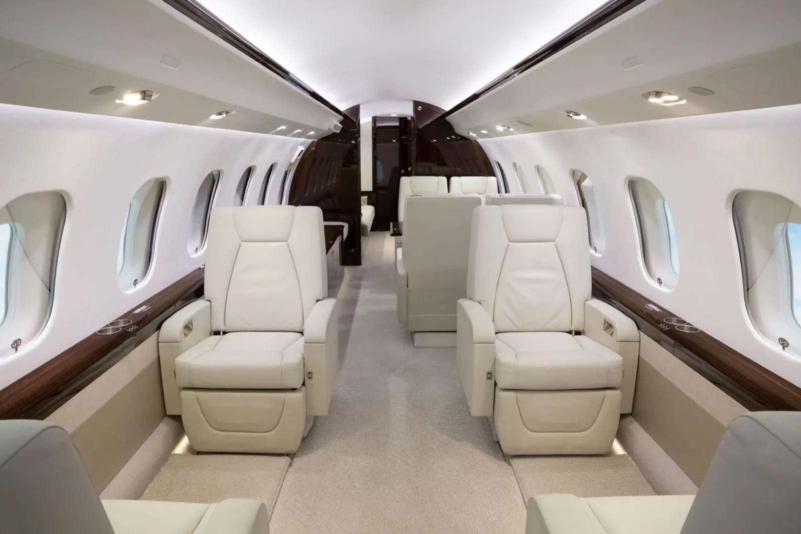 A spacious aircraft cabin featuring rows of individual white leather seats and dark wood trim.