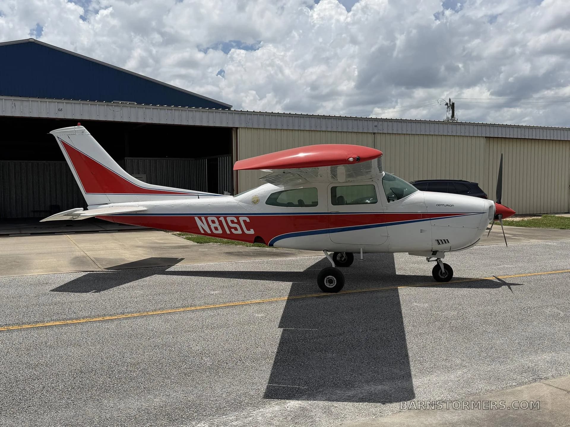 A side view of a white and red Cessna 210 Centurion aircraft, registration N81SC, parked on an asphalt ramp.