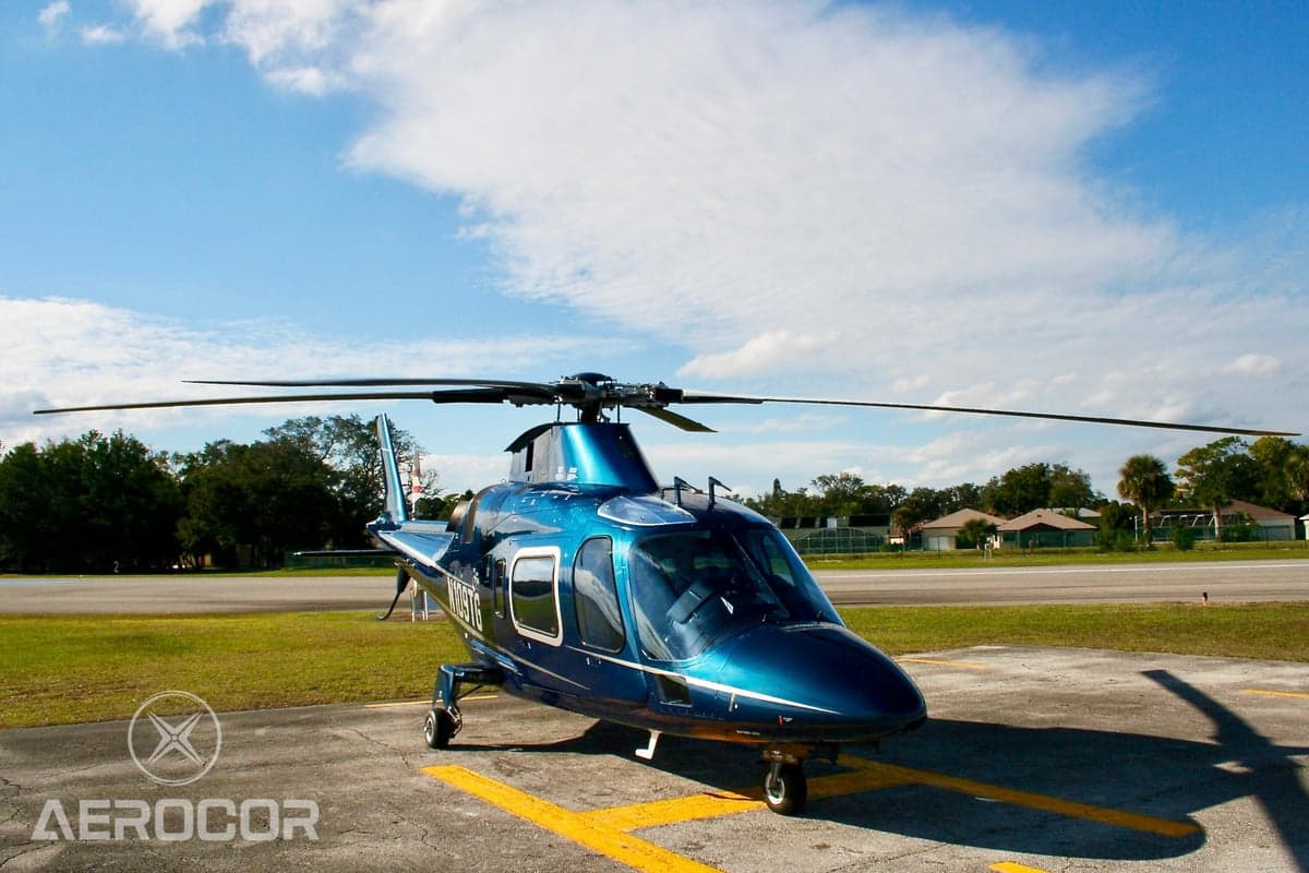Three-quarter front view of a blue AgustaWestland AW109 helicopter (N109TG) parked on an airfield.