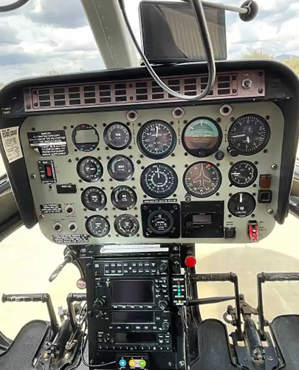 The instrument panel and controls of a helicopter cockpit, featuring multiple gauges and a display screen.