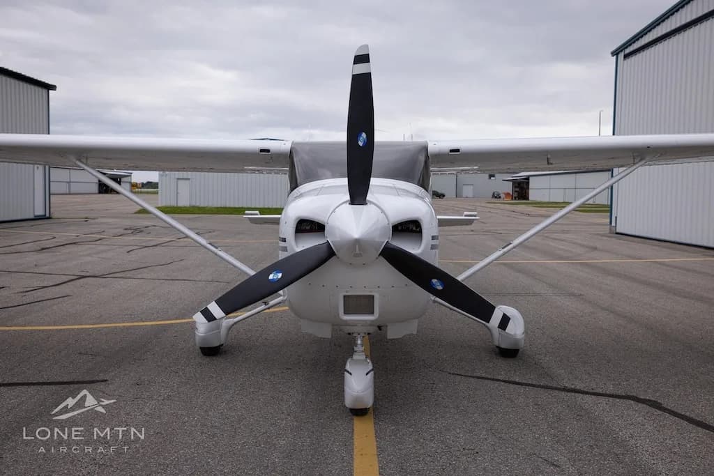 A head-on view of a white Cessna 182 Skylane with a black propeller, parked on an asphalt ramp.