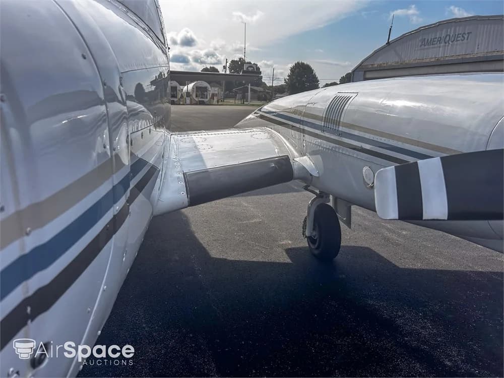 A close-up view of the right side of a white Piper Navajo fuselage and engine nacelle with blue and gold stripes.