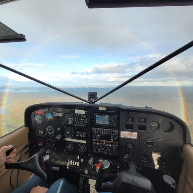 View of the instrument panel from the cockpit of an aircraft with a rainbow in the distance.