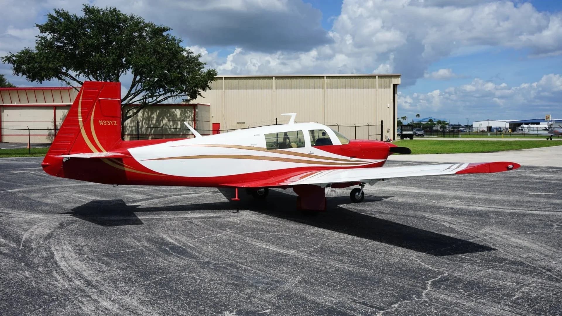 A red and white single-engine aircraft, N33YZ, is parked on an asphalt apron with a hangar in the background.