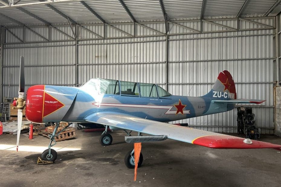 A light blue and red aircraft, registration ZU-CWM, is parked inside a hangar.