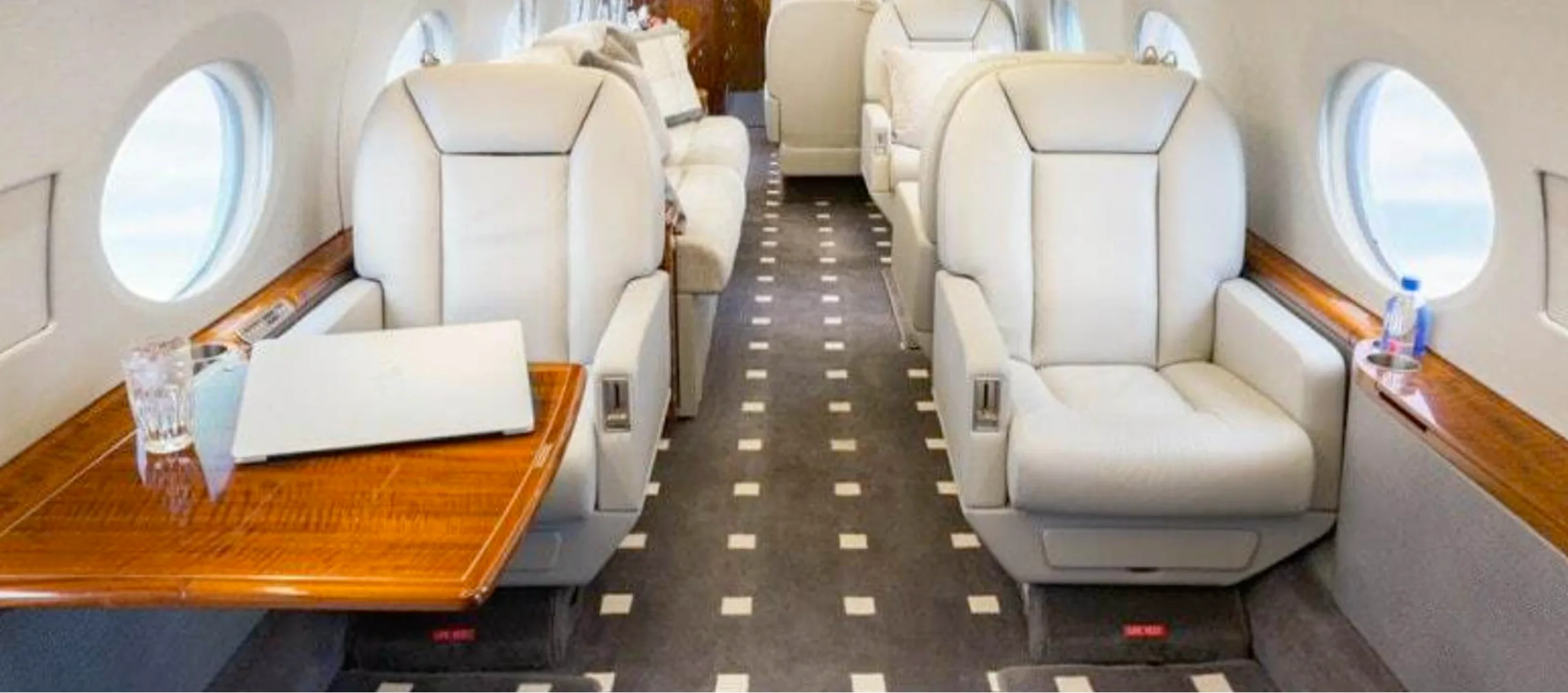 A view of the aircraft's interior with white leather seats and a wooden table.