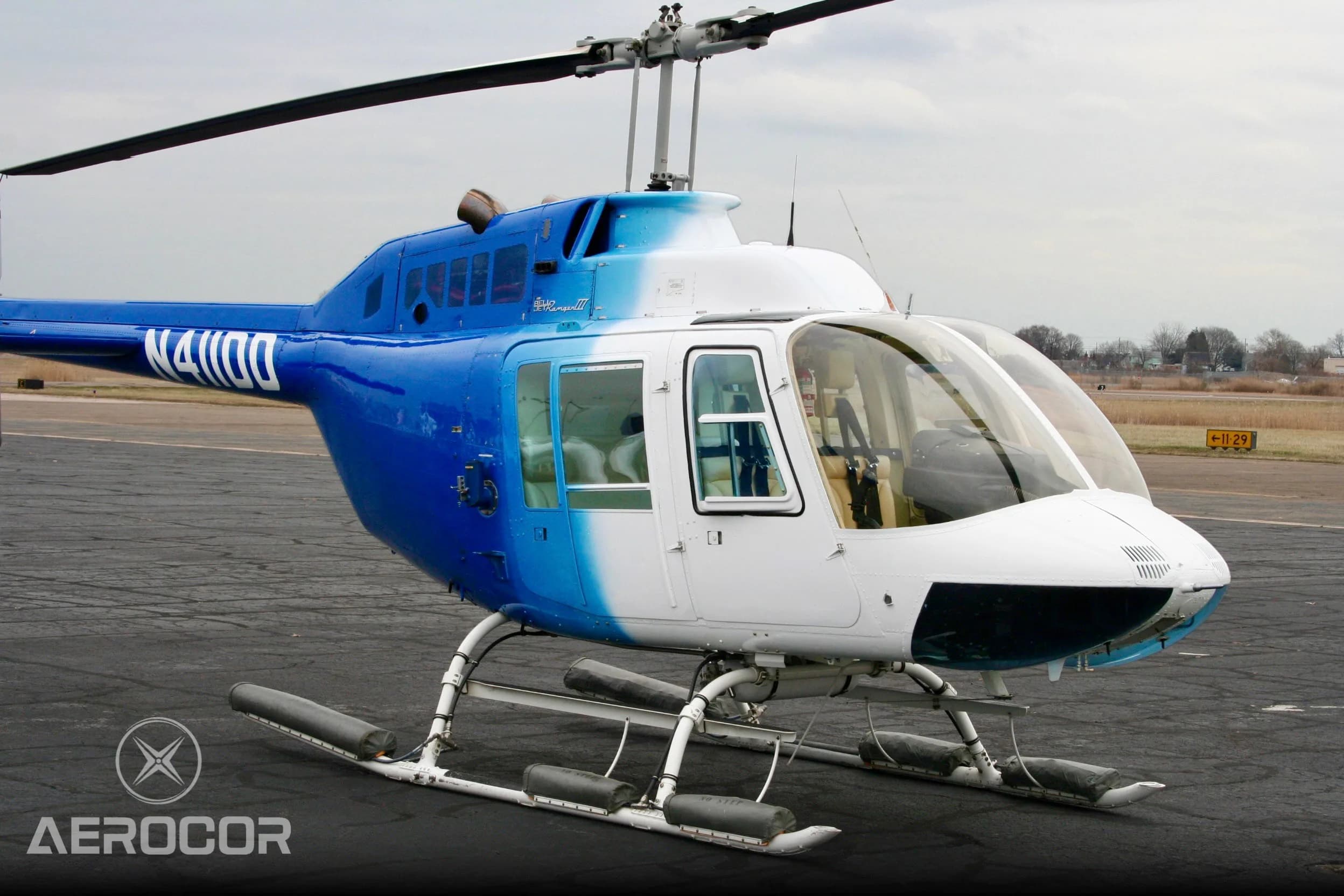 A front three-quarter view of the blue and white Bell JetRanger III helicopter, tail number N411DD, parked on an airport tarmac.