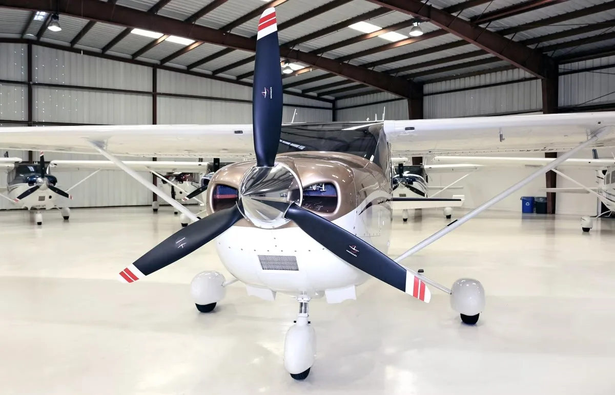 A head-on view of the brown and white Cessna Skylane N875PJ with its propeller, parked in a hangar.