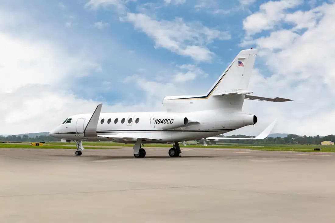 A Falcon jet sits on the tarmac with mountains in the background.