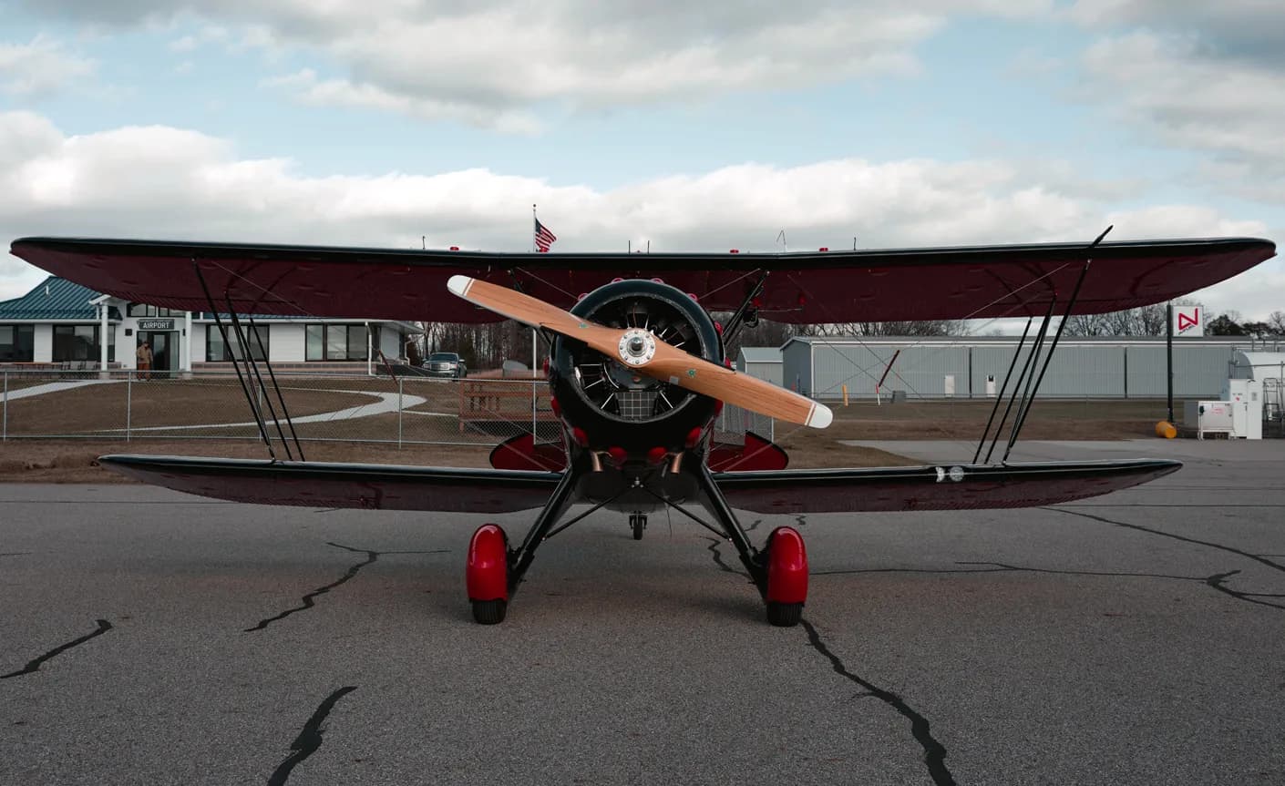 Front view of a black and red biplane with a wooden propeller.