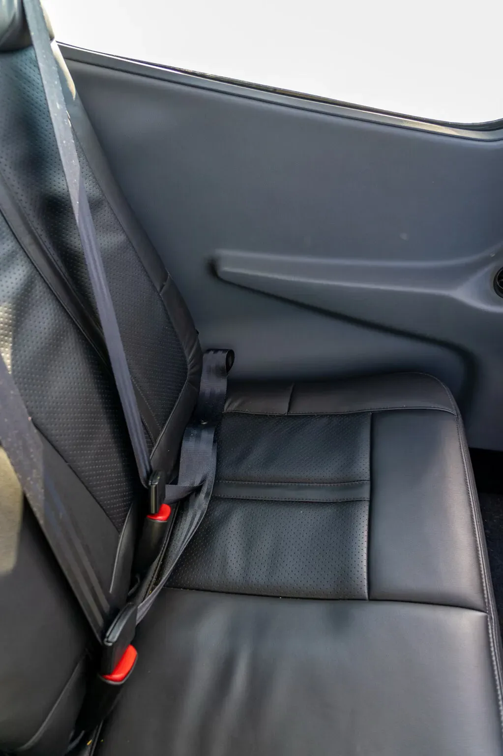 A close-up view of a black leather aircraft seat and side panel.