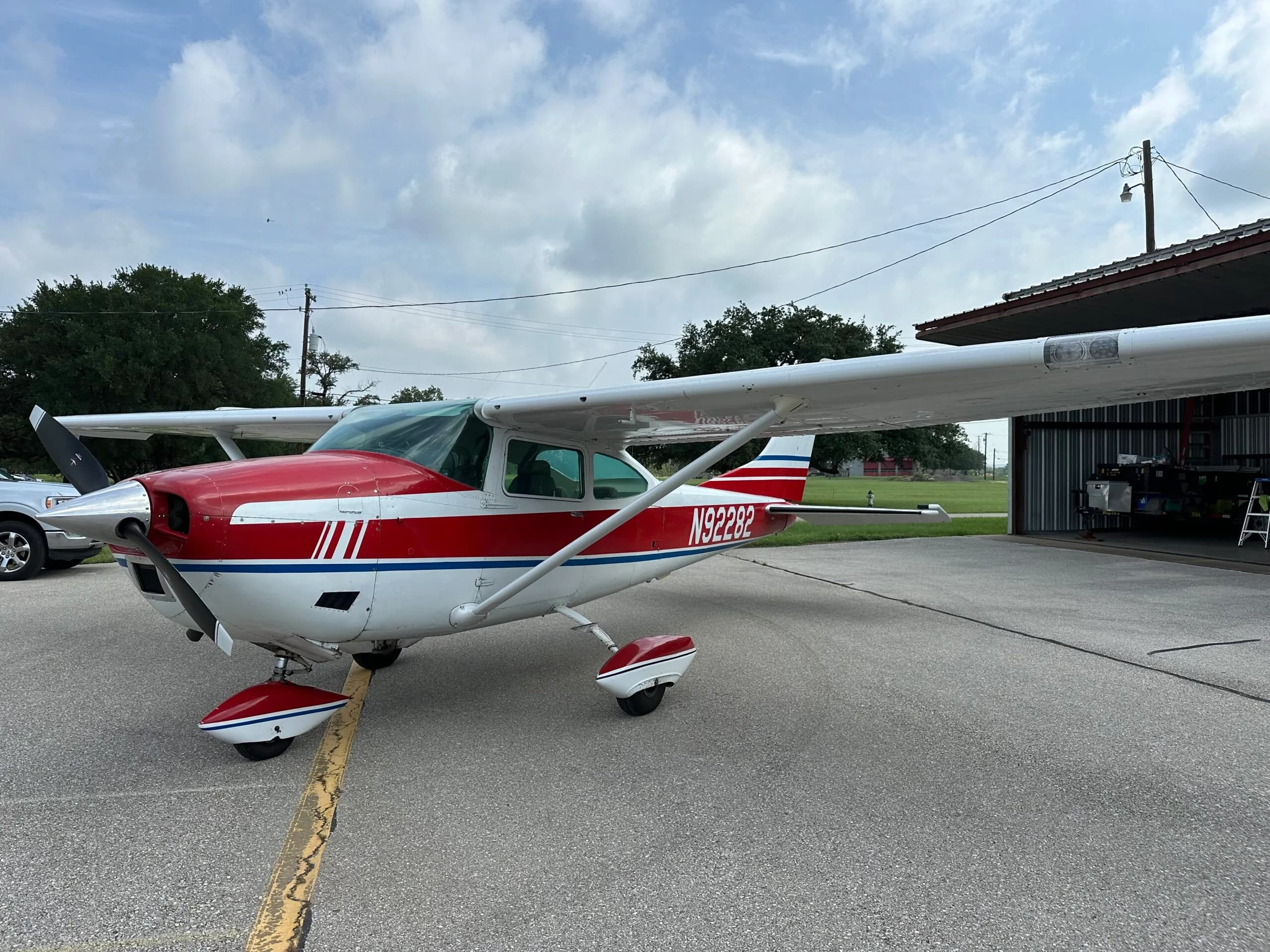 A white and red single-engine propeller aircraft (N92282) parked on an asphalt ramp with a hangar in the background.