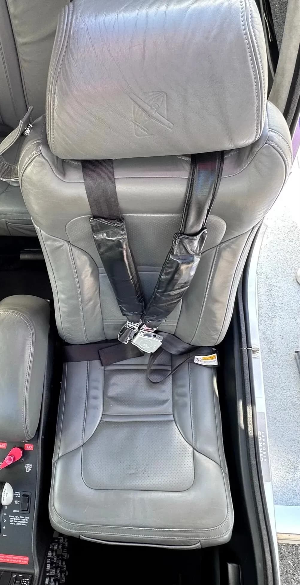 A grey leather pilot's seat with a five-point harness inside the aircraft cabin.