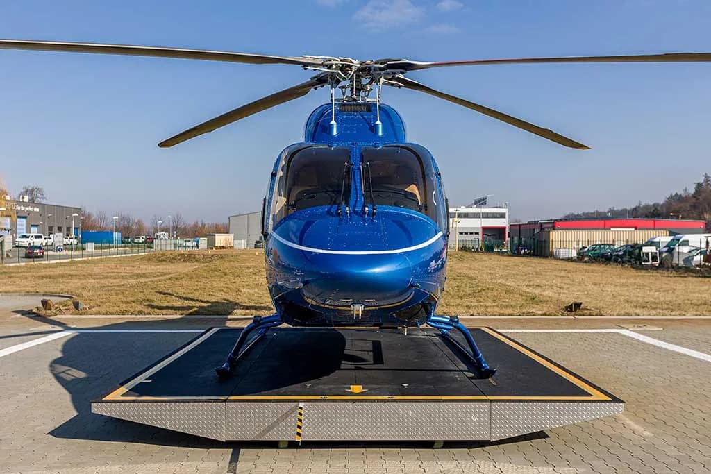 A front view of a blue helicopter with white stripes, registration OM-TIP, on a helipad.