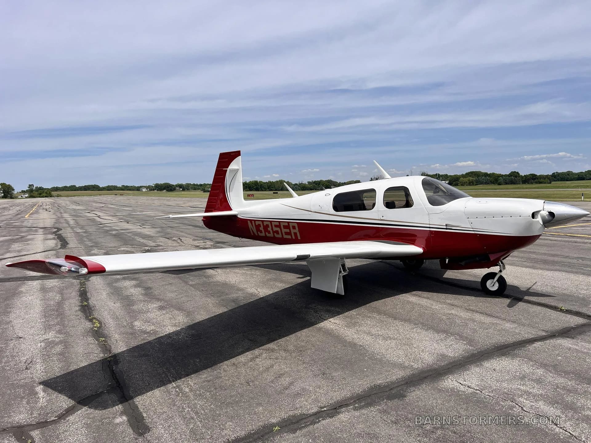 A side view of a white and red single-engine propeller aircraft with tail number N335ER parked on an airfield.
