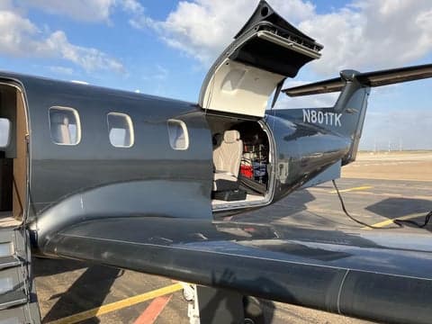 Exterior view of a dark gray jet with the door open, showing the interior.