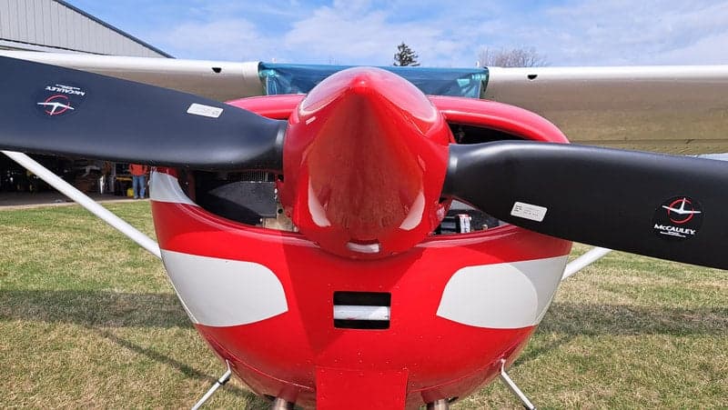 Close-up of the propeller and nose of a red and white Cessna aircraft.