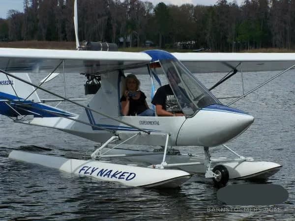 A white and blue experimental floatplane with two people inside, floating on a lake.