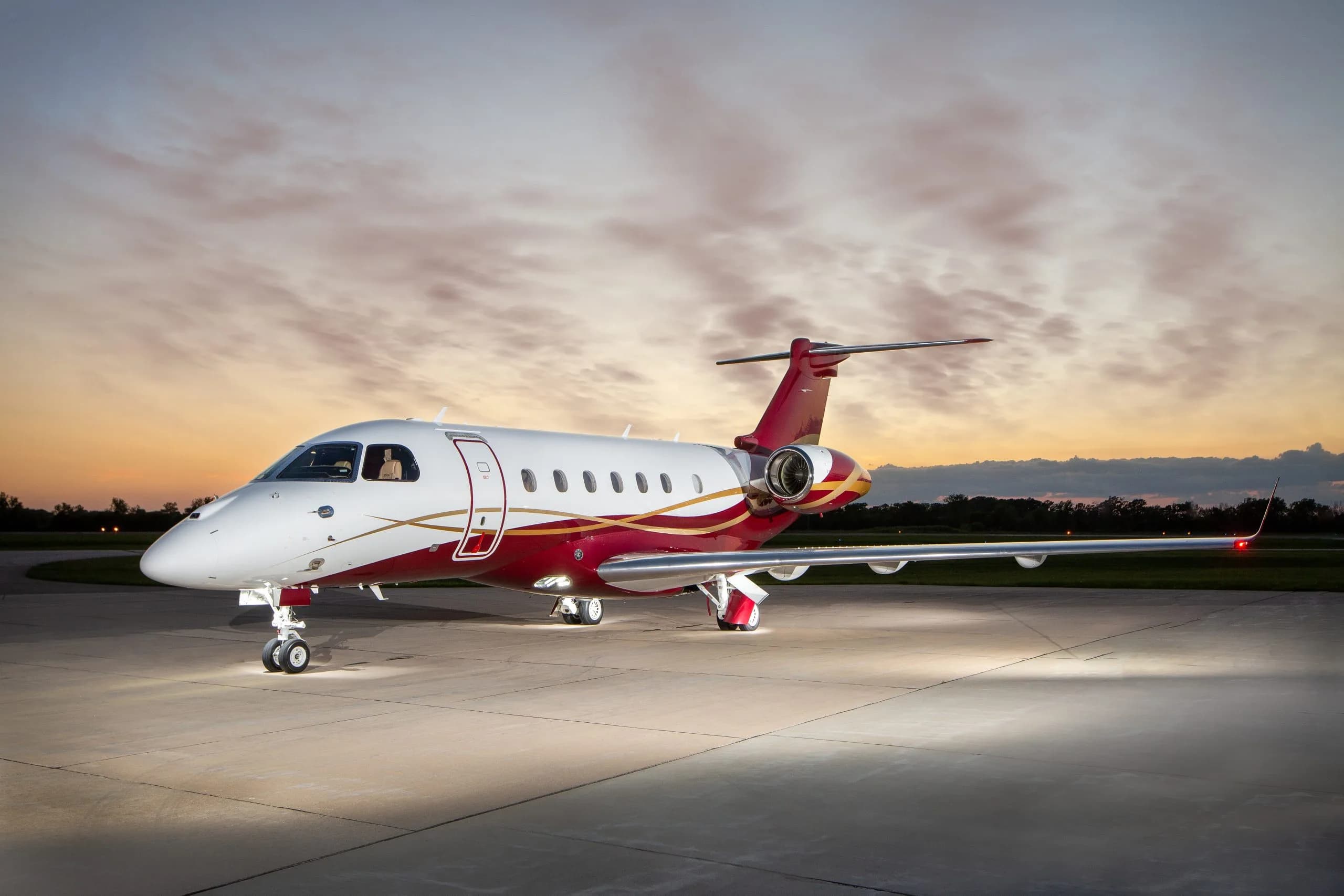 A white and red Embraer Phenom 300E on the tarmac at dusk.