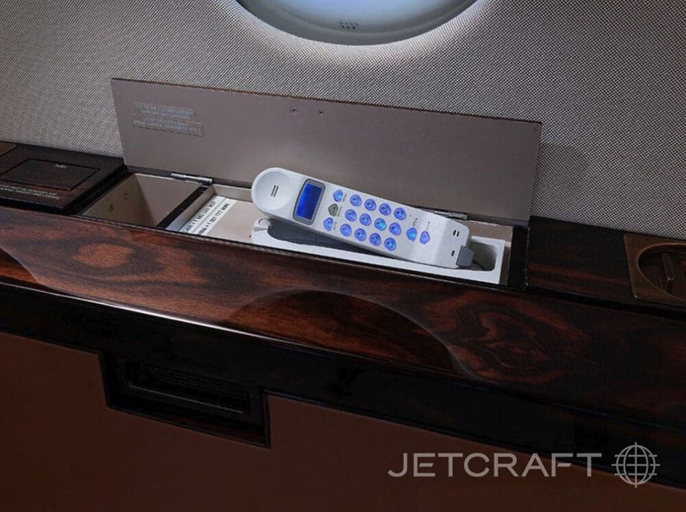 Aircraft cabin with a telephone in a compartment.