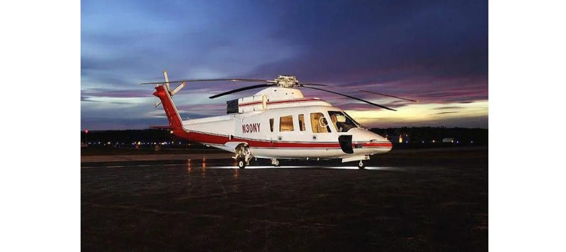 A white and red helicopter with registration N30NY sits on the tarmac at dusk.