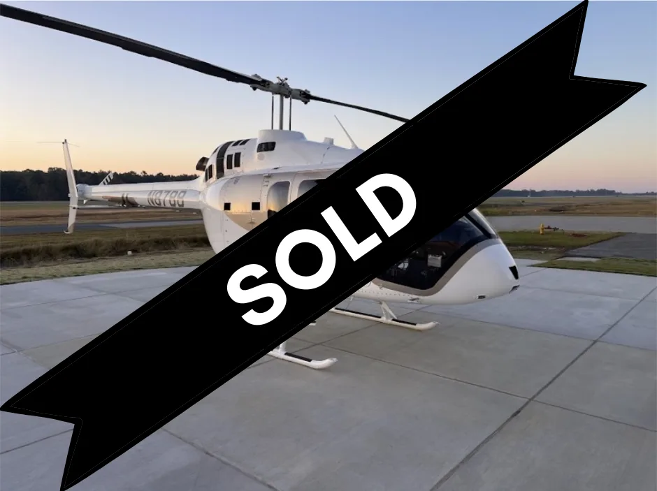 A white helicopter with registration N8799 is parked on a concrete pad at an airfield during sunset.