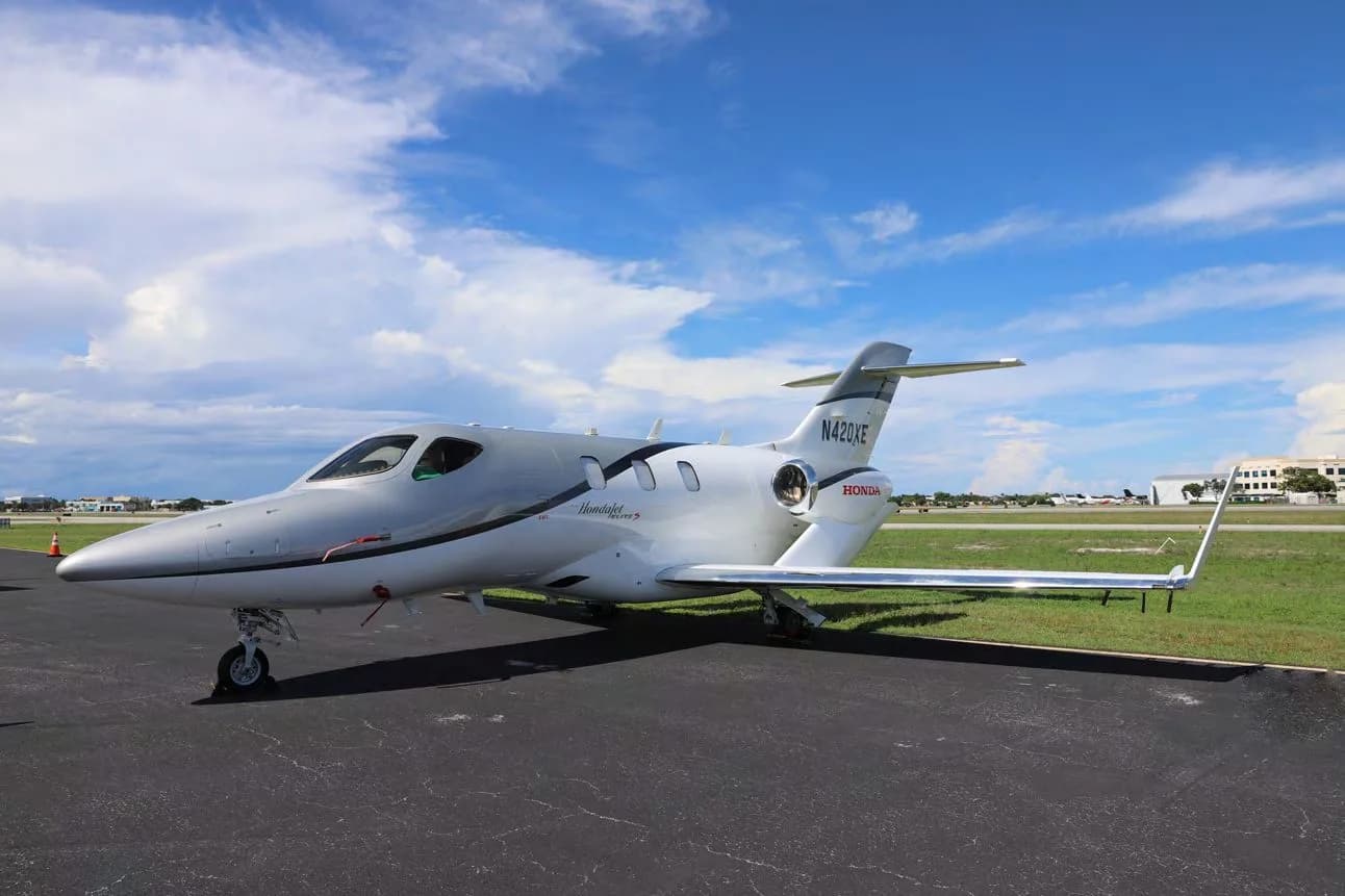 A white and grey HondaJet Elite S (N420XE) parked on a tarmac under a blue sky with clouds, viewed from the front-right.