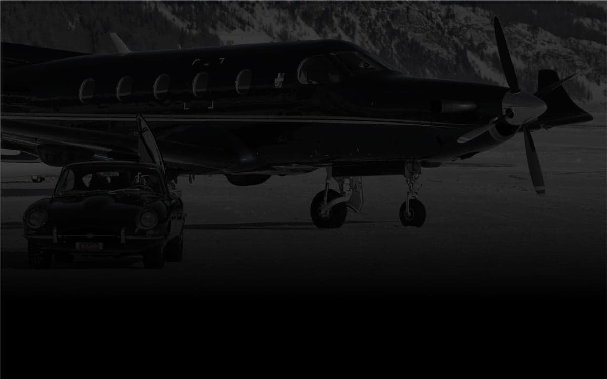 A dark-colored aircraft parked on a snowy surface with a classic car in front.