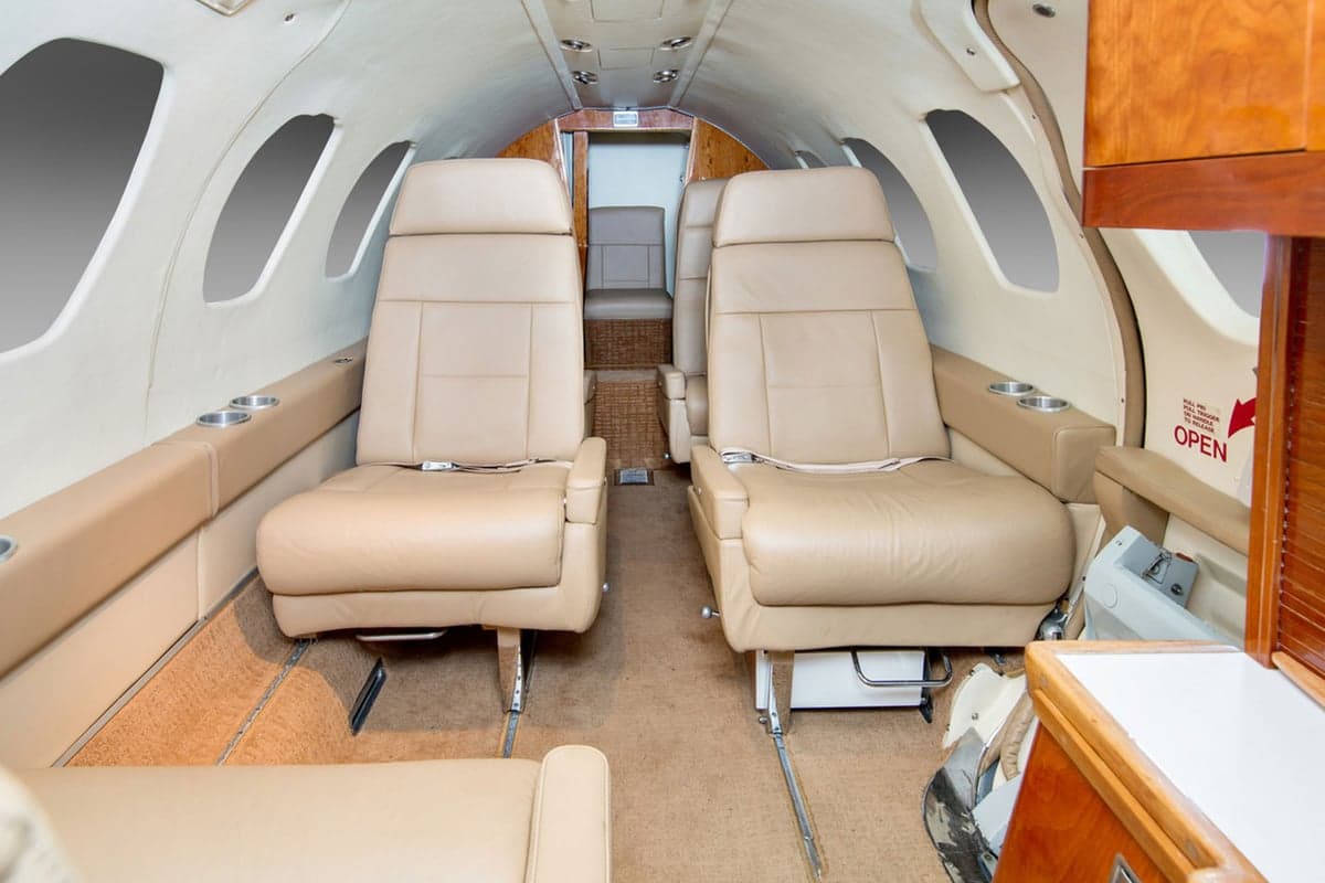 The aircraft cabin interior with two rows of beige leather seats and wood paneling.