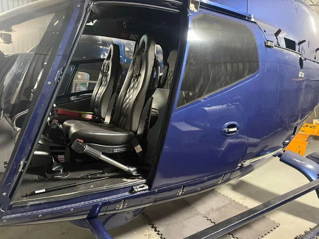 The open door of a blue helicopter reveals two black bucket seats in the cabin.