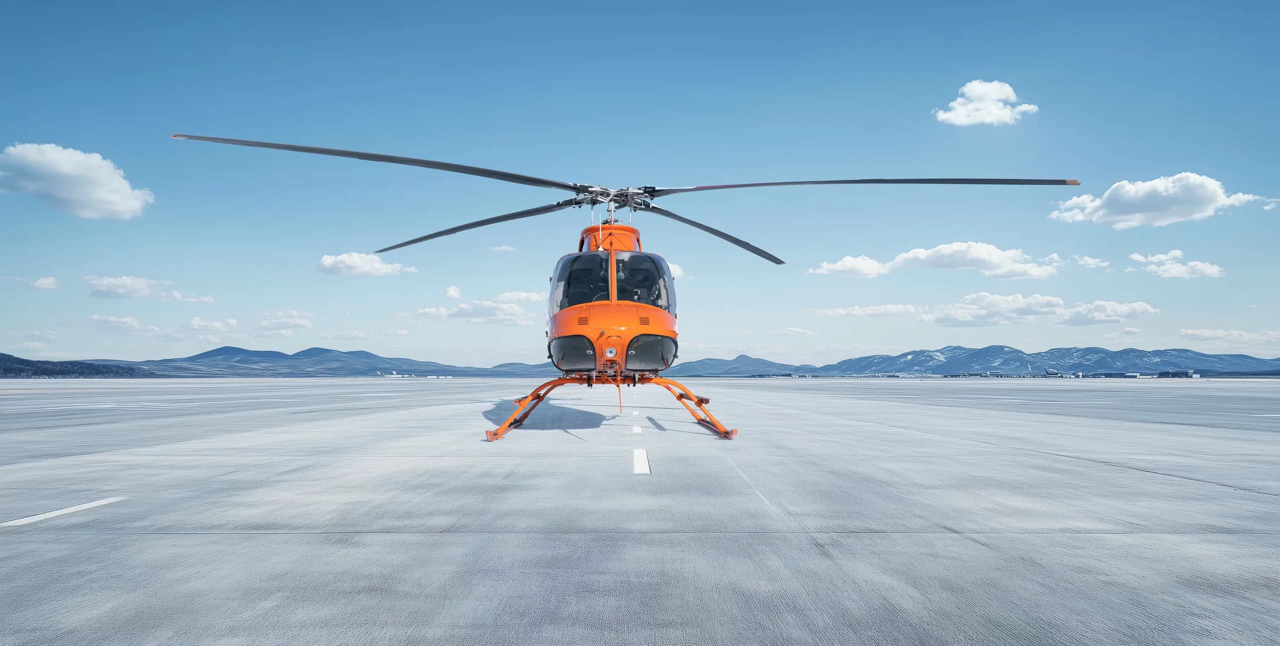 A Bell 407 helicopter with an orange and white paint scheme is parked on a concrete surface.