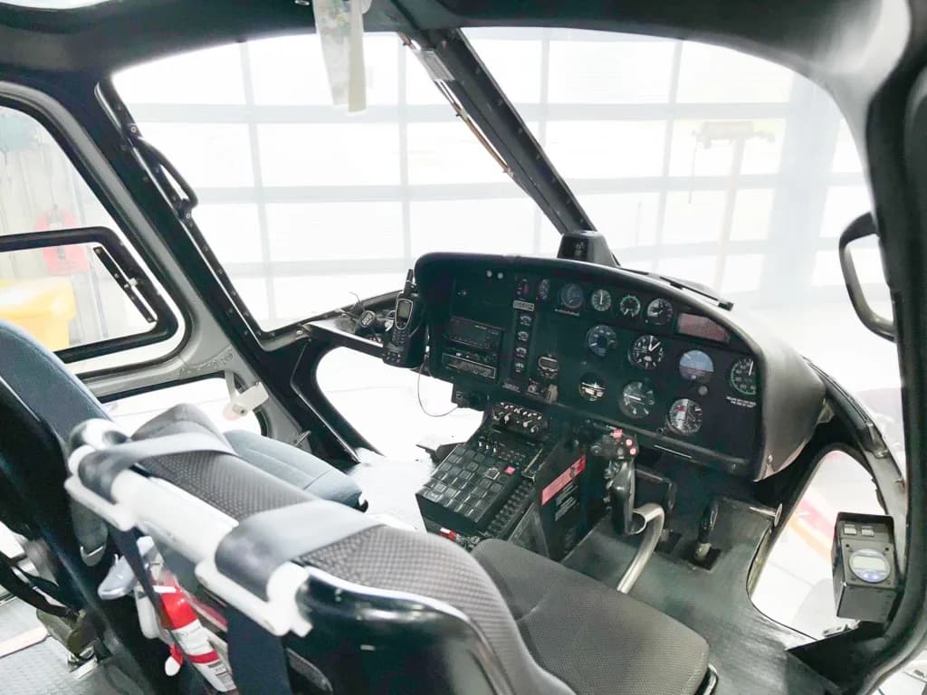 The cockpit of a helicopter showing the instrument panel, controls, and pilot's seat.