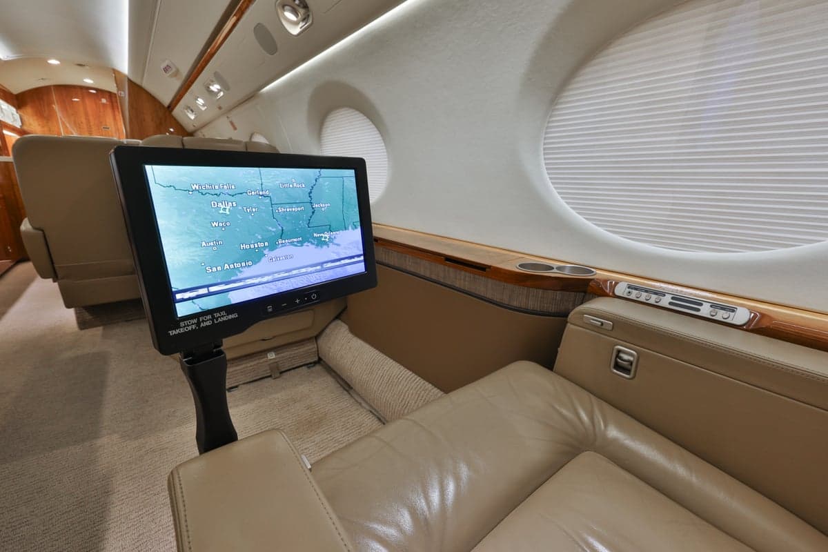Interior view of the aircraft cabin with a leather seat and a monitor displaying a map.