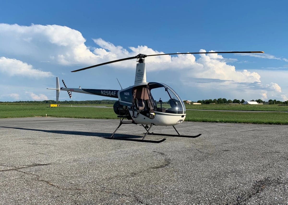 A Robinson R22 helicopter, tail number N2584F, sits on the tarmac under a blue sky with fluffy clouds.