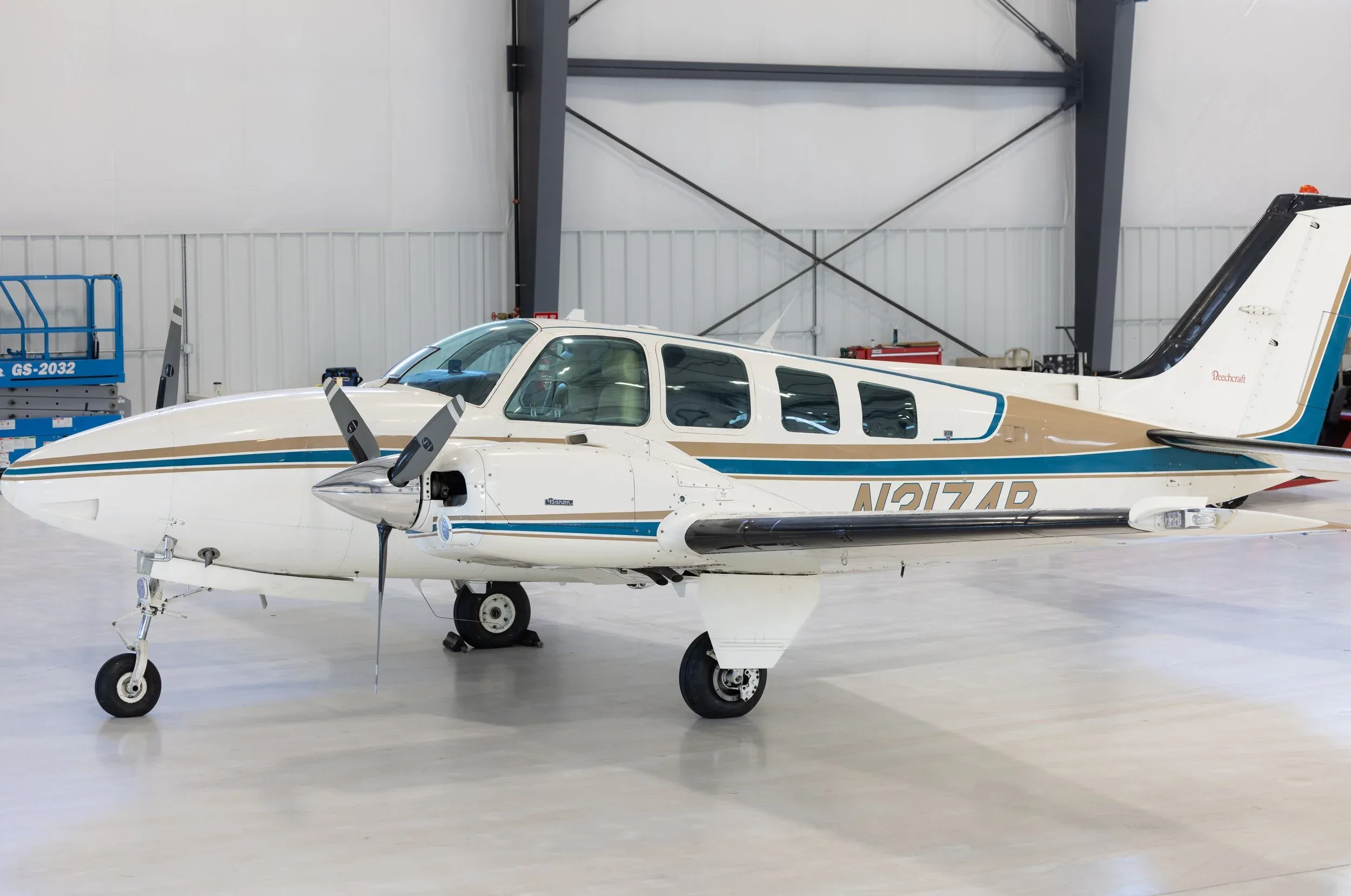 Side view of a white and tan Beechcraft Baron aircraft with registration N2174D inside a hangar.