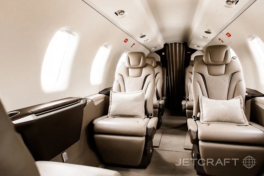 The luxurious tan leather interior cabin of a private jet with multiple passenger seats and windows.