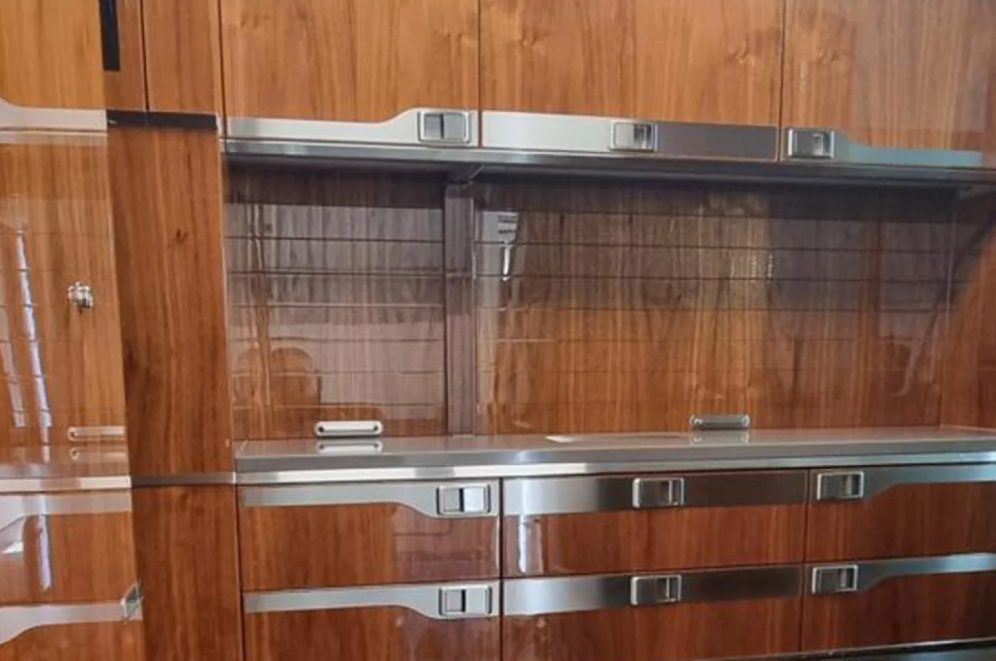 A close-up of polished wood cabinetry with silver accents and handles, likely part of a galley or storage unit within an aircraft interior.