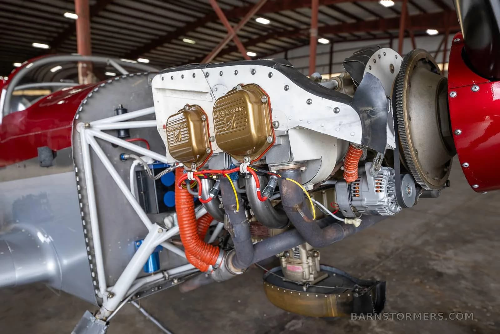 A close-up view of the exposed engine of the red and silver experimental aircraft, showing cylinders and exhaust pipes.