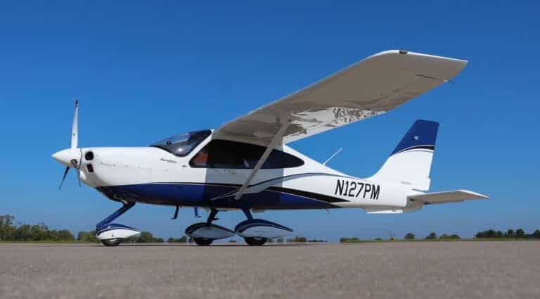 Side view of a white and blue single-engine propeller aircraft N127PM on an airfield.